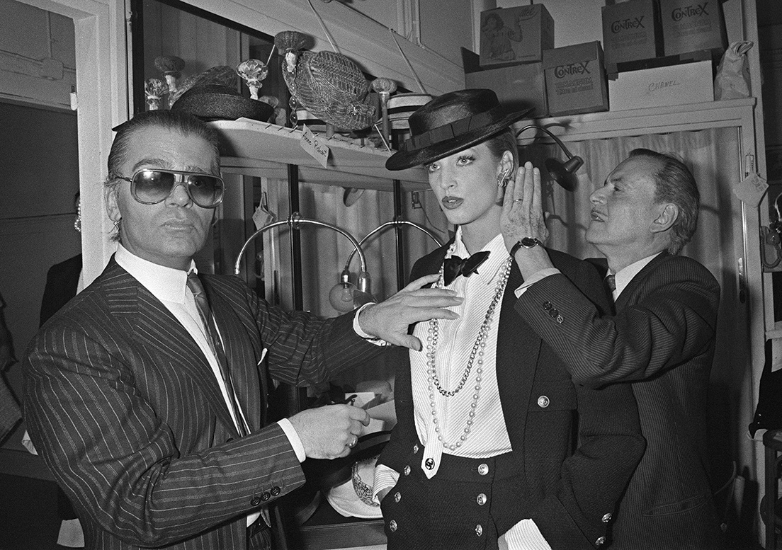 На этом снимке, сделанном 24 января 1983 года, немецкий модельер Карл Лагерфельд (слева) и парикмахер-стилист корректируют наряд модели во время своей первой весенней летней коллекции Chanel