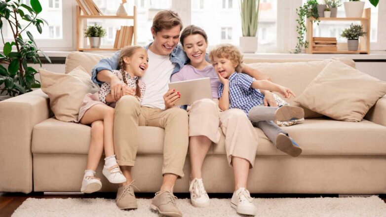 Семья на диване смотрят фильм Young joyful casual family of two kids and couple sitting on sofa and watching funny video