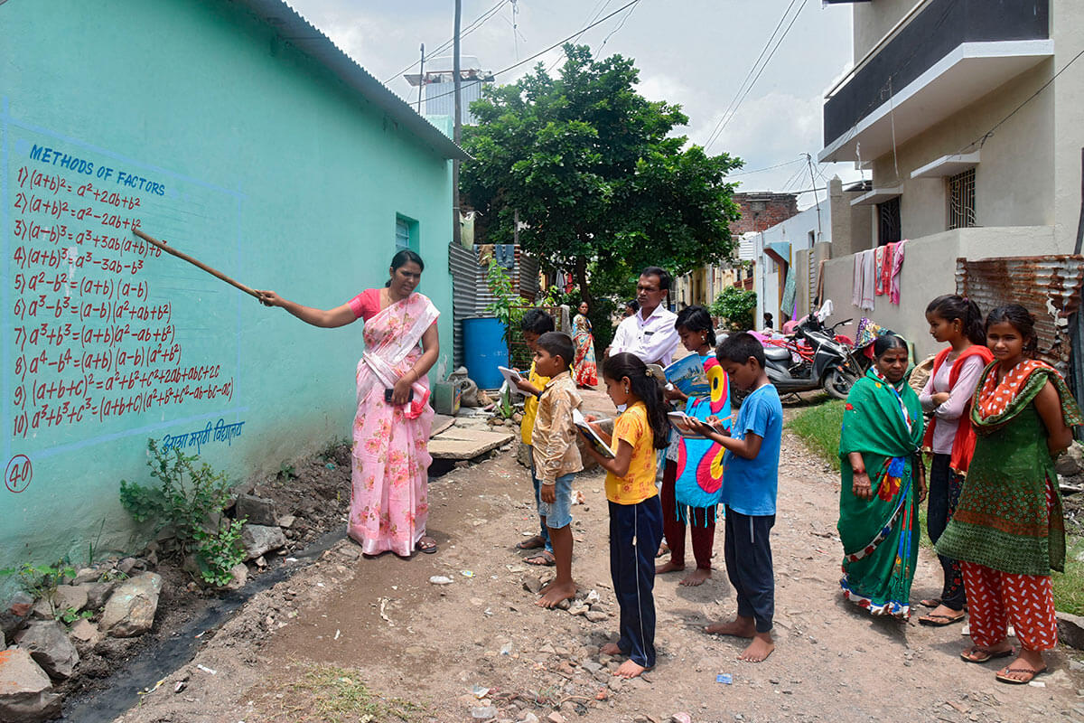 Учитель дает урок на стене дома для школьников из бедных районов в Индии