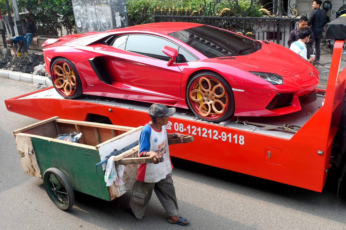 Мужчина везет тележку мимо автомобиля Ferrari в Джакарте