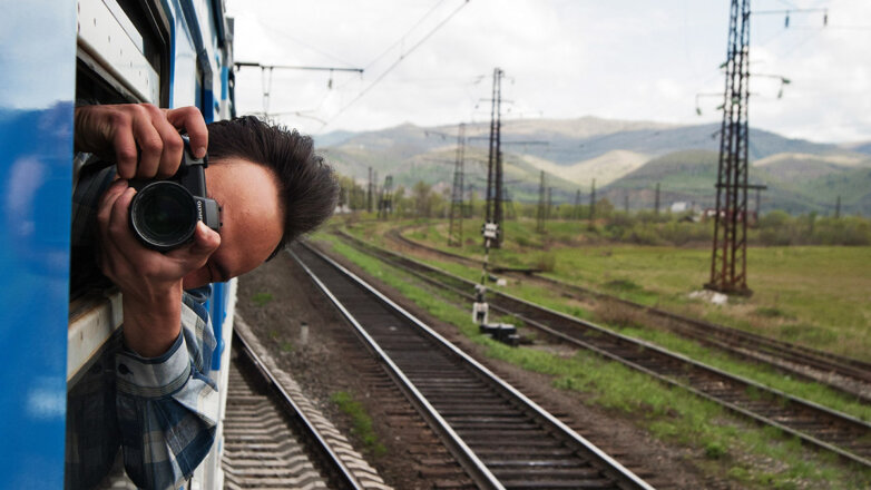 Мужчина из окна поезда фотографирует пейзаж