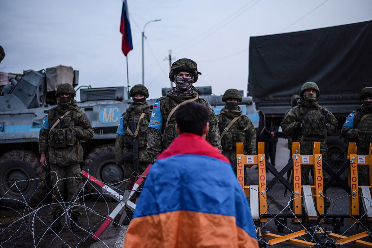 Протестующий с национальным флагом Армении стоит перед российскими миротворцами, блокирующими дорогу возле Степанакерта