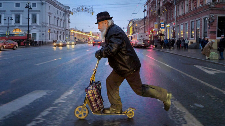 Пожилой мужчина едет на самокате по пешеходному переходу