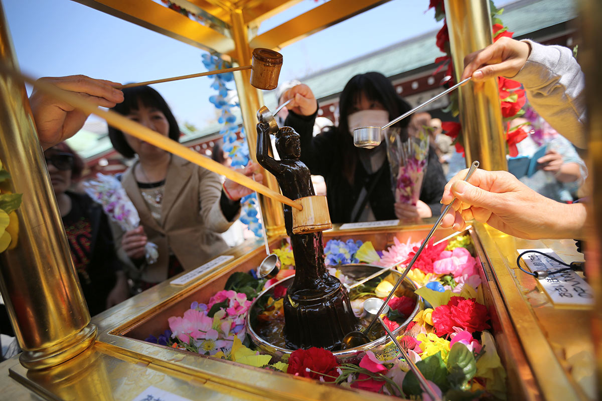 Посетители поливают водой статую маленького Будды в честь дня рождения Будды в Токио