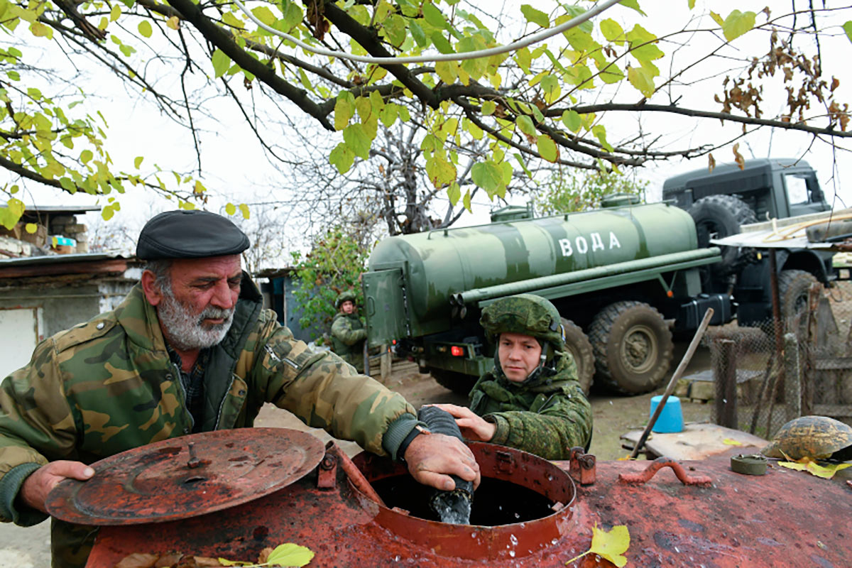 Российский миротворец с местным жителем наполняют бочку водой в Нагорном Карабахе
