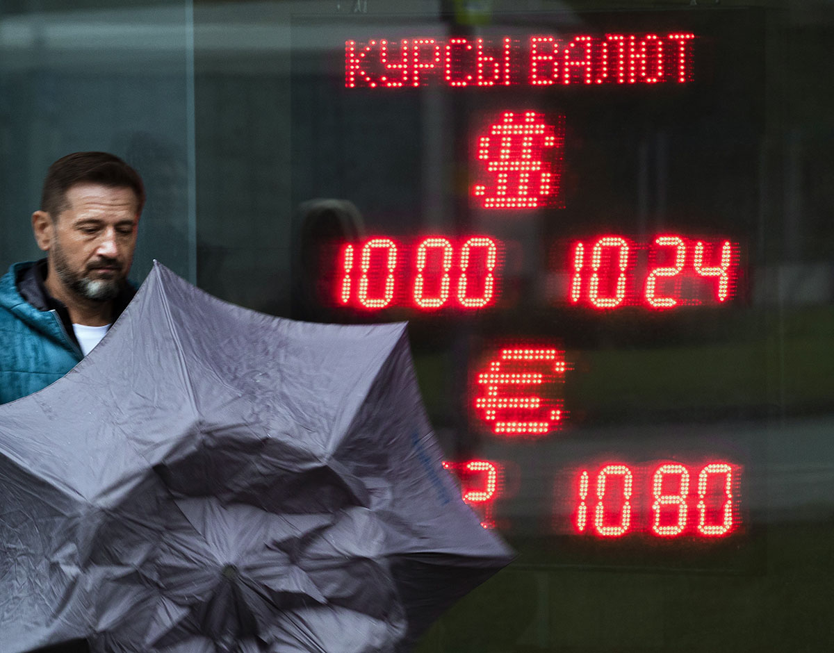 Мужчина с зонтом на фоне электронного табло с курсами валют