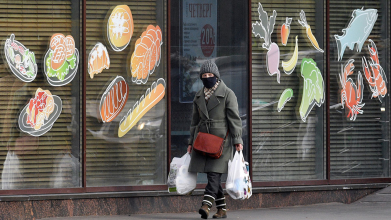 Женщина с покупками у витрины продуктового магазина