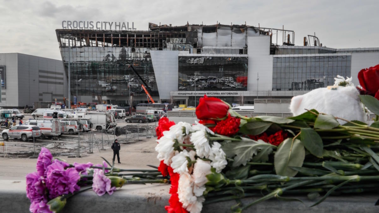 Цветы в память о погибших при теракте на фоне сгоревшего здания концертного зала 