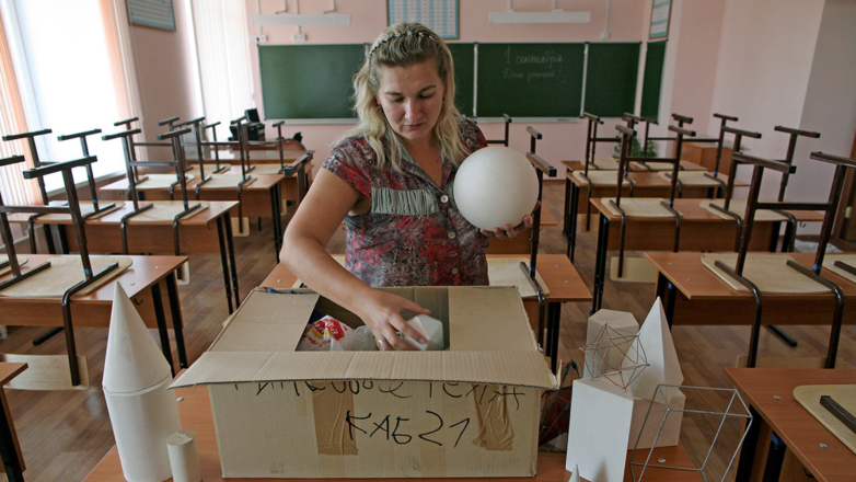 Учитель достает из коробки геометрические фигуры в классе математики