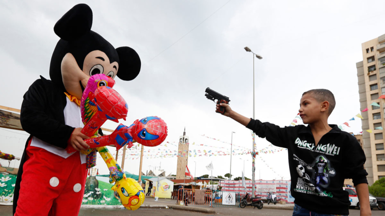 Мальчик направляет игрушечный пистолет на человека в костюме Микки Мауса