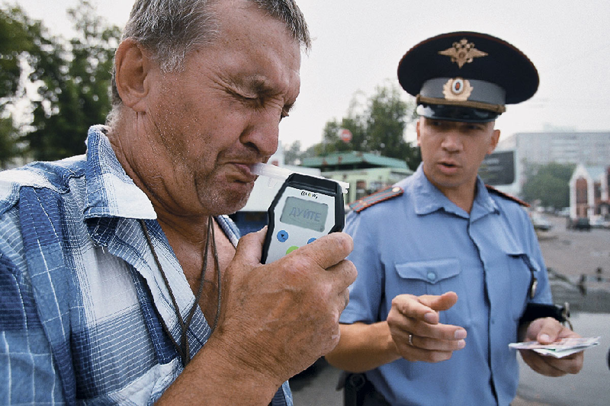 Сотрудник ГИБДД проверяет водителя автомобиля с помощью алкотестера