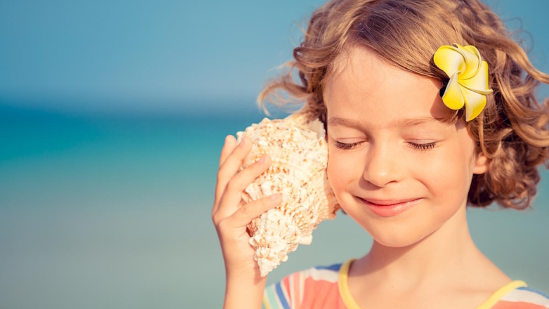 Девочка слушает шум моря в морской раковине