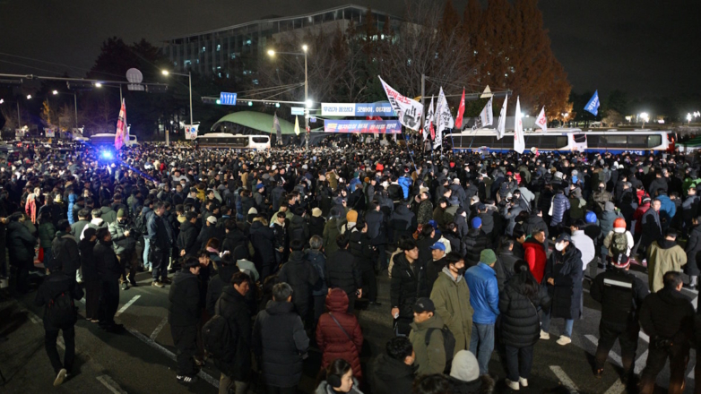 Протестующие против введения военного положения перед зданием парламента в Сеуле