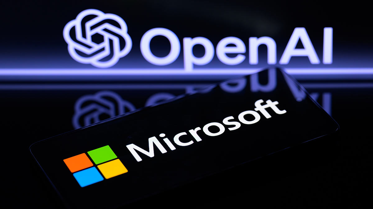 Логотип Microsoft отображается на смартфоне, а на заднем плане на экране виден логотип OpenAi.